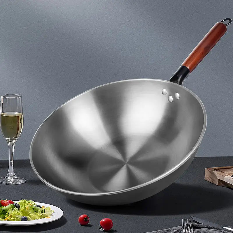 Wok aus Schmiedeeisen mit Antihaftbeschichtung, Edelstahlgehäuse, Holzgriff und drei kleinen Nieten am Rand.