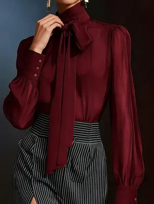 A rich burgundy satin puff sleeve blouse featuring a high collar and a flowing bow at the neckline.