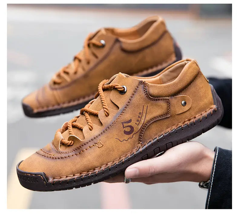 Herren-Lederschuhe im britischen Casual-Stil mit Schnürung aus beigem Wildleder mit braunen Schnürsenkeln, dunkler Gummisohle, gestickten Details und einem geprägten „5 1976“-Logo an der Seite.