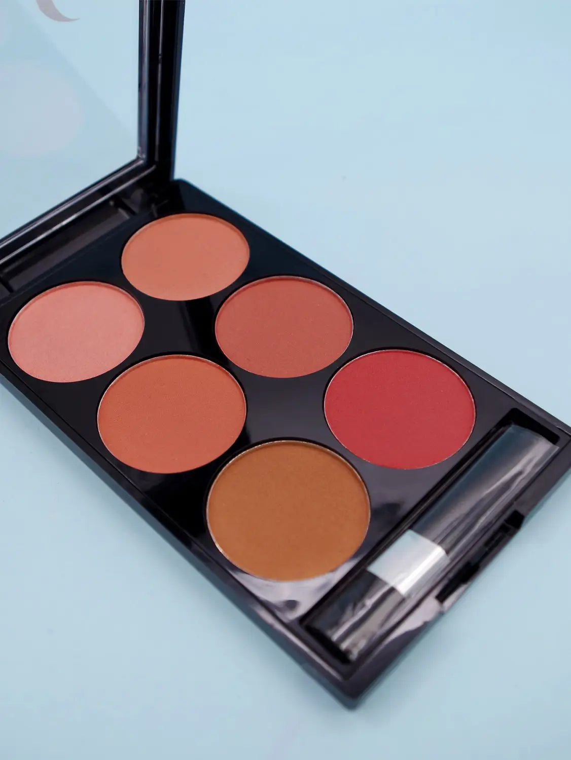 Palette compacte de fard à joues noir en six couleurs, présentant six godets circulaires aux teintes pêche terracotta et rouge chaudes pour le kit de contour du visage en V.