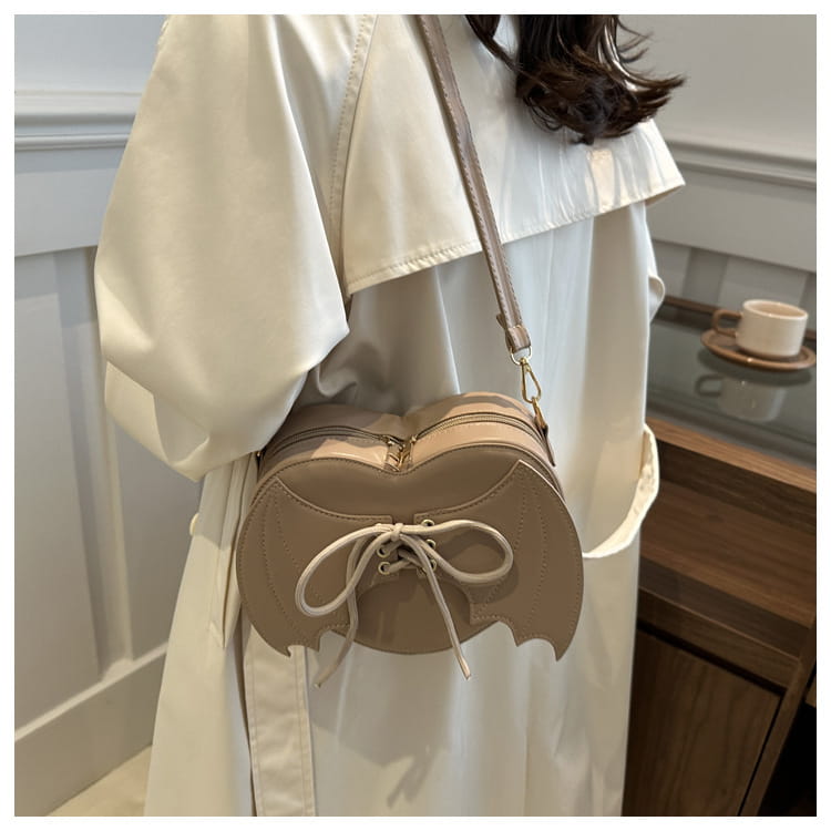Beige bat wing heart crossbody bag made of leather with lace up front detail.