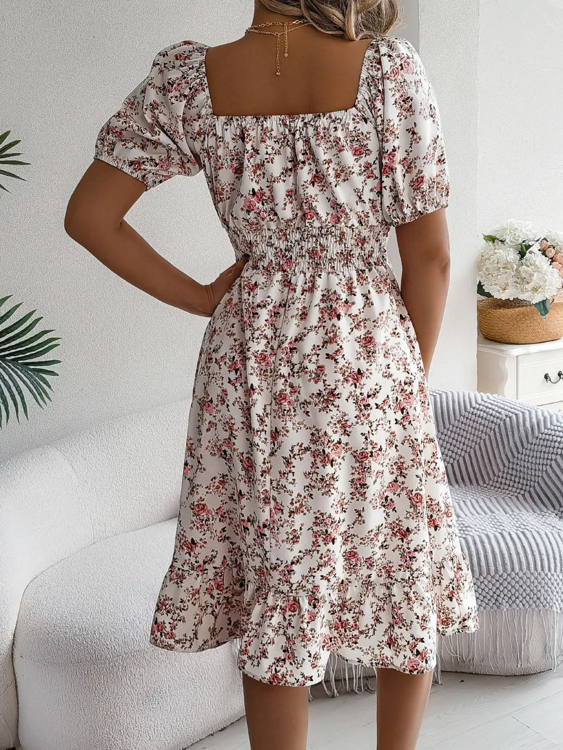 Une femme portant une robe d’été blanche à imprimé floral à encolure carrée, manches bouffantes et détails à volants, avec taille élastiquée.