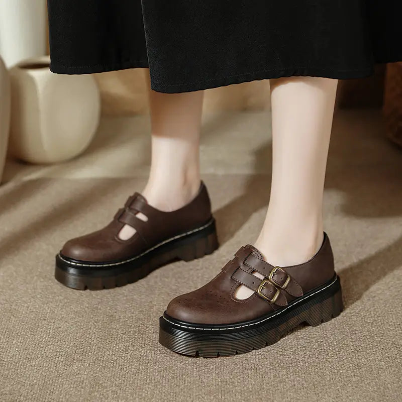 Braune Ledermary-Jane-Schuhe mit dicker schwarzer Gummisohle und zwei Messing-Schnallen, im Kontrast zum Produkttitel schwarze Lederschnürstiefeletten auf Plattform im Brogue-Mary-Jane-Stil