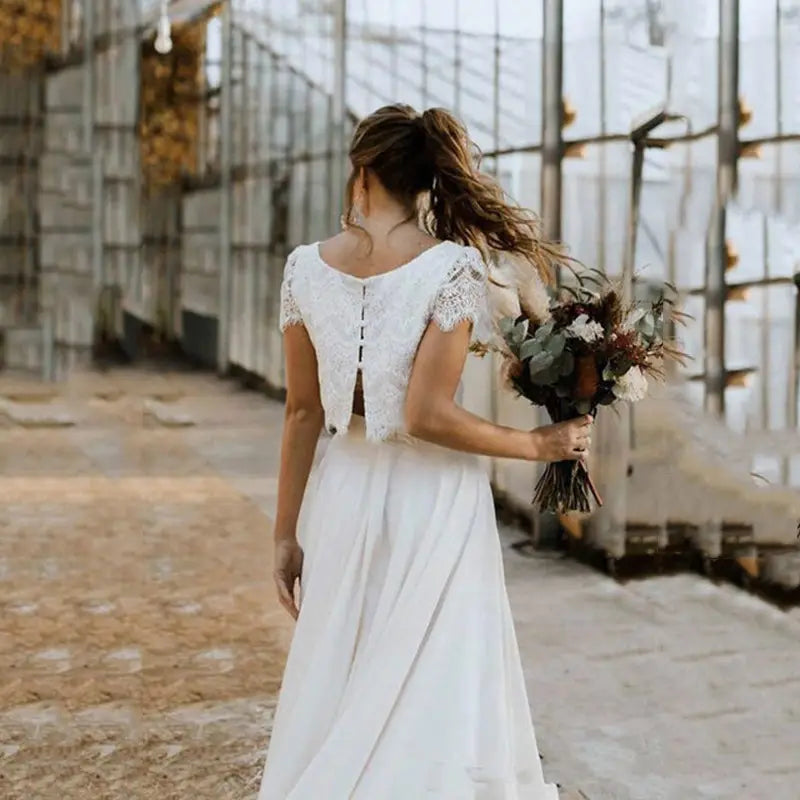 Robe de mariée en dentelle blanche et satin à manches courtes, décolleté bijou, présentée de dos, avec un détail de fermeture éclair.
