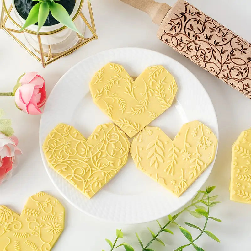 Biscuits en forme de cœur jaunes en relief, ornés de motifs de feuilles et de vignes complexes, réalisés au moyen d’un rouleau à pâtisserie en bois de hêtre en relief floral pour la cuisson.