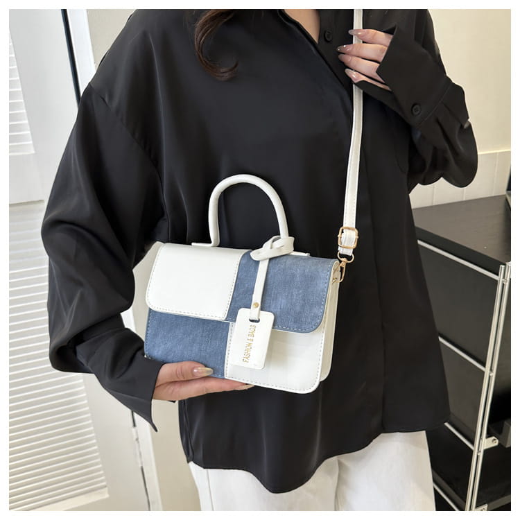 A two tone denim patchwork crossbody bag featuring white leather and blue denim panels with a matching white handle and strap.