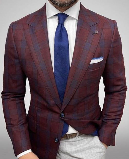 Ein maßgeschneiderter Herren-Karos-Blazer Slim Fit in Burgunderrot und Navy mit dezenter Struktur, passenden Knöpfen und einem ordentlich gefalteten Einstecktuch für den lässigen Einsatz.