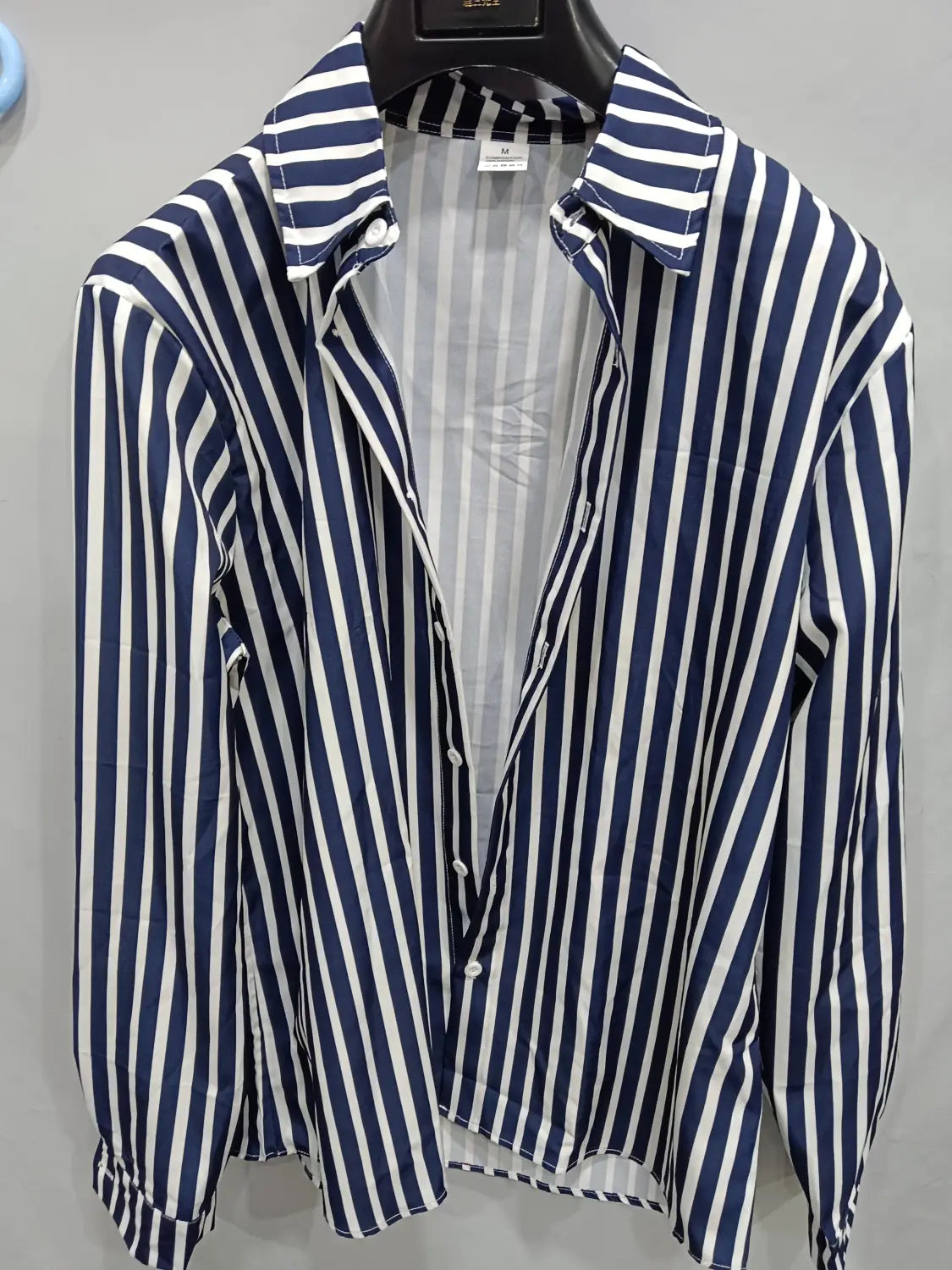 Chemise décontractée à manches longues rayée verticalement bleu marine et blanc pour hommes, avec col classique, suspendue sur un cintre noir.