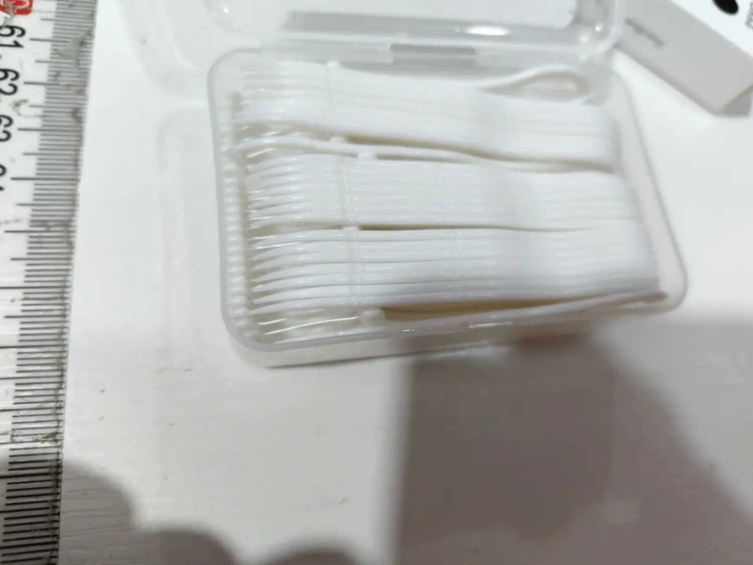 petits cure-dents en plastique blanc disposés de manière ordonnée dans une boîte de rangement transparente pour fil dentaire avec étui à ouverture automatique
