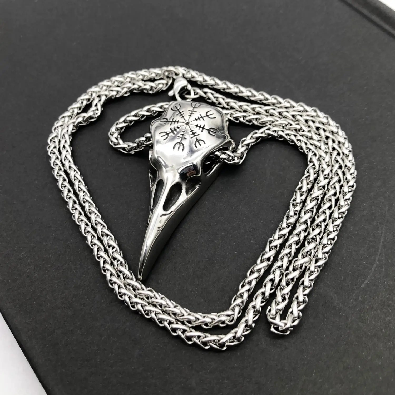 Silver vintage Viking runic raven skull pendant on a braided stainless steel chain necklace.