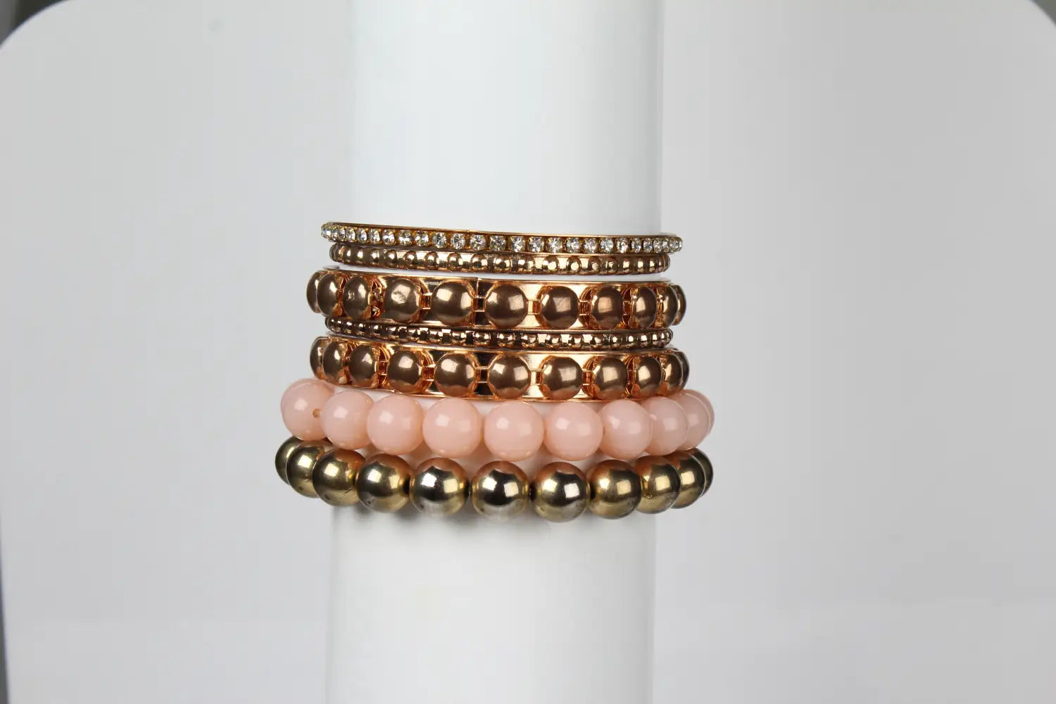 Stack of five gold-toned beaded bracelets with a top band adorned in clear crystals from the retro gold and pink rhinestone bangle bracelet set.