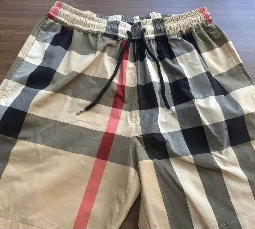 Men’s striped tropical print swim trunks featuring beige navy blue gray and red checkered pattern with elastic waistband and black drawstrings.
