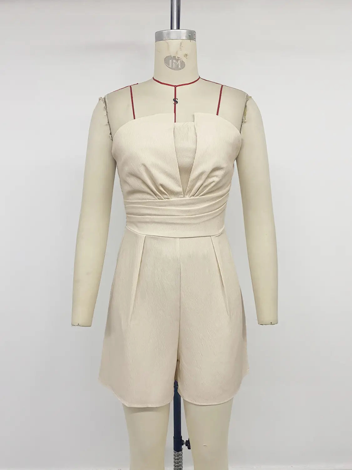 Cream strapless pleated jumpsuit in beige satin with a ruched bodice and pleated shorts.