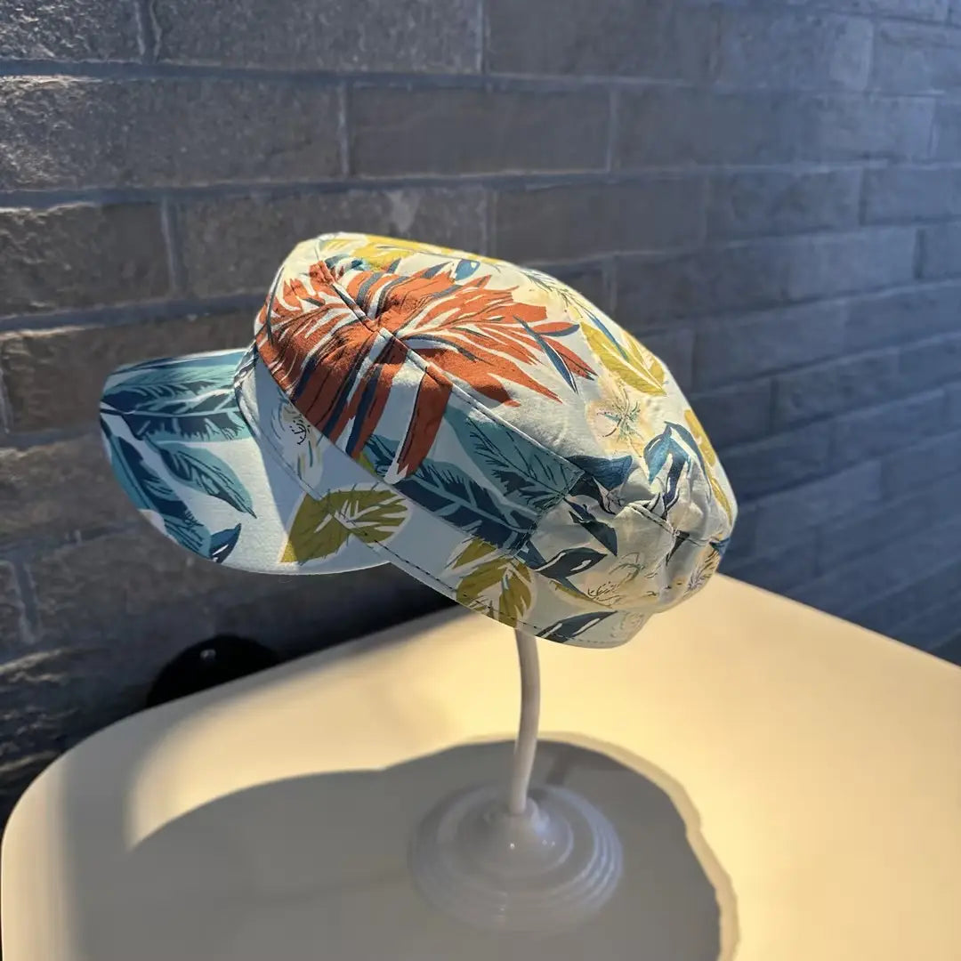 Gorra tipo bucket hat floral, estilo coreano, impresa, con un estampado tropical vibrante, patrones de hojas en naranja, teal y amarillo audaces sobre una base de tela clara.