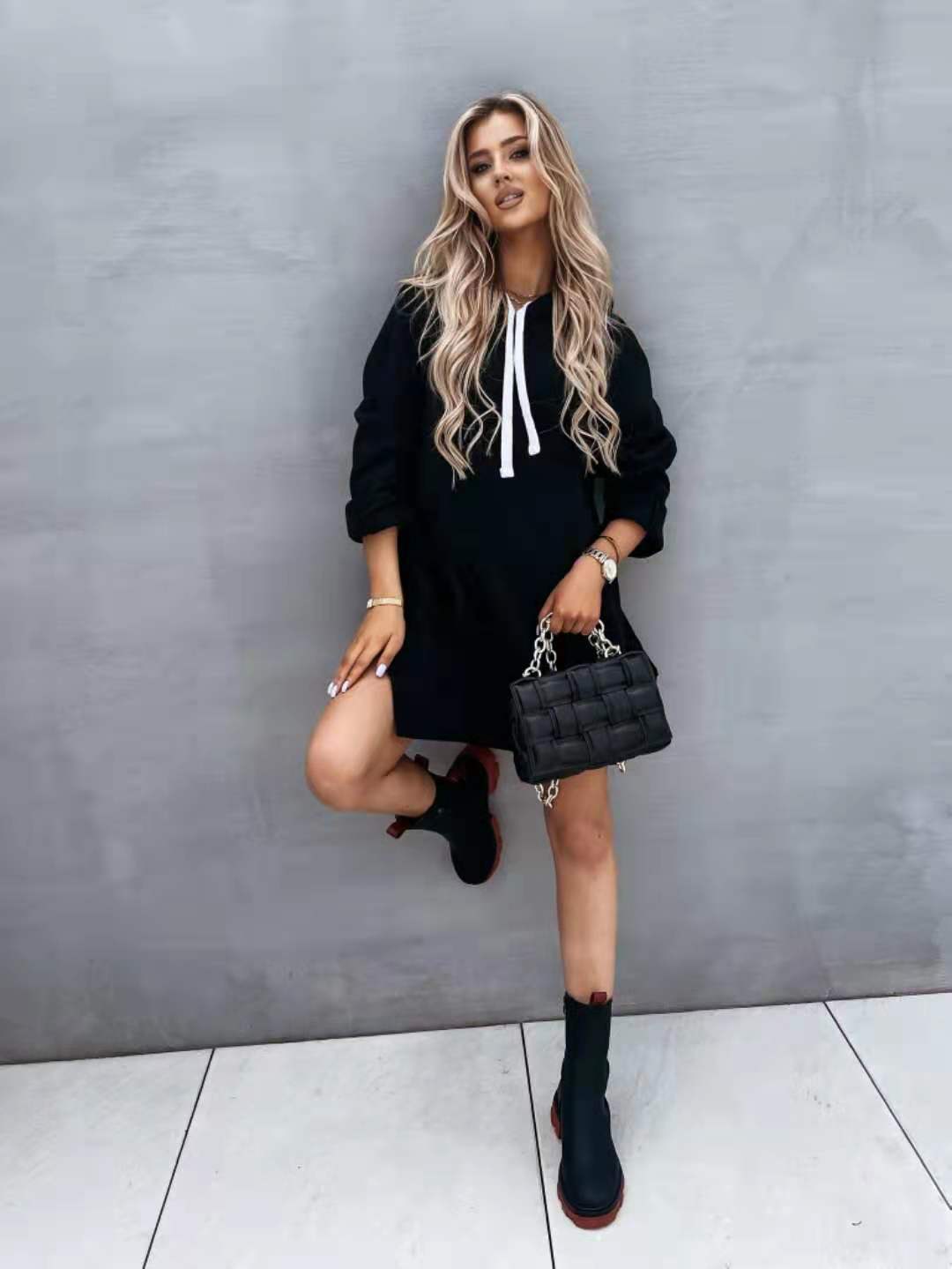 Black quilted leather handbag with silver chain strap displayed alongside an oversized mid length hooded sweatshirt dress with pockets.