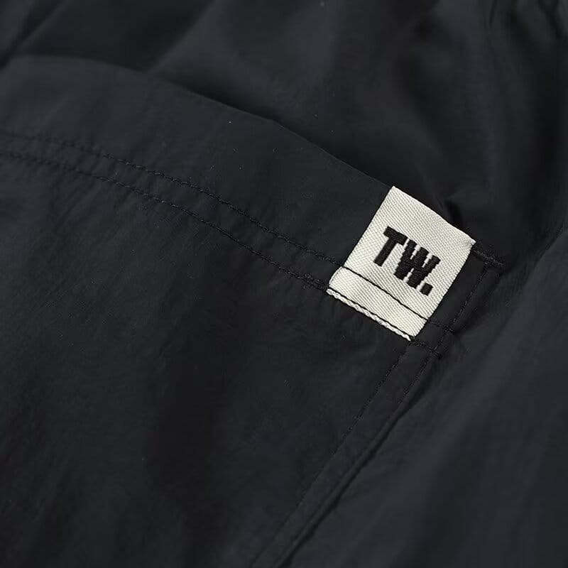 Shorts en nylon décontractés pour hommes, coupe droite, présentant une veste en nylon noire avec une étiquette tissée blanche brodée du marquage tw sur l’avant.