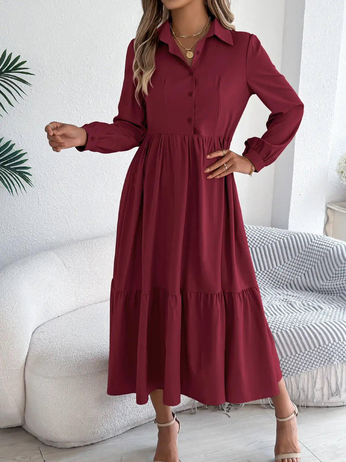 A woman wearing a long sleeve button down midi dress in rich burgundy fabric with tiered ruffles at the hem.
