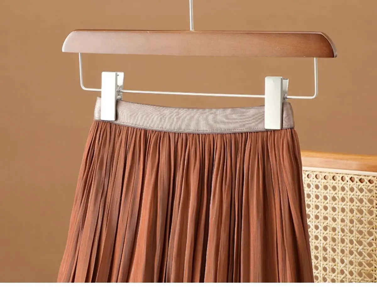 Ein rostfarbener irrisierender Chiffon-Faltenrock mit gerafftem Bund, der an einem Holzkleiderbügel hängt.