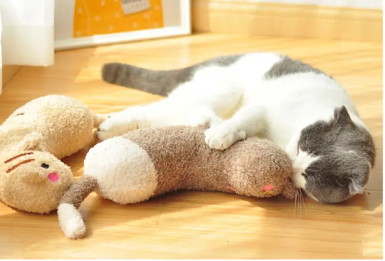 Eine graue und weiße Katze, die auf einem Plüsch-Katzenkissen ruht, geformt wie eine weiche braune Fellmaus mit rosiger Nase, ausgelegt für Nackenunterstützung und Gelenkentlastung.