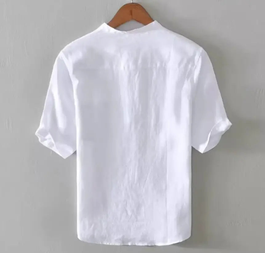 Chemise ample en lin blanche à col mandarin de style japonais rétro, à manches courtes, coupe détendue et texture subtile, suspendue à un cintre en bois.