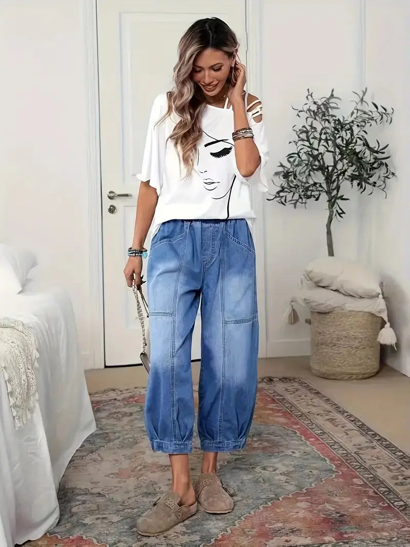 Femme portant un jean capri rétro à taille haute, effet wash clair, associé à un t-shirt graphique blanc décolleté sur les épaules et à des mocassins d’appoint beiges.