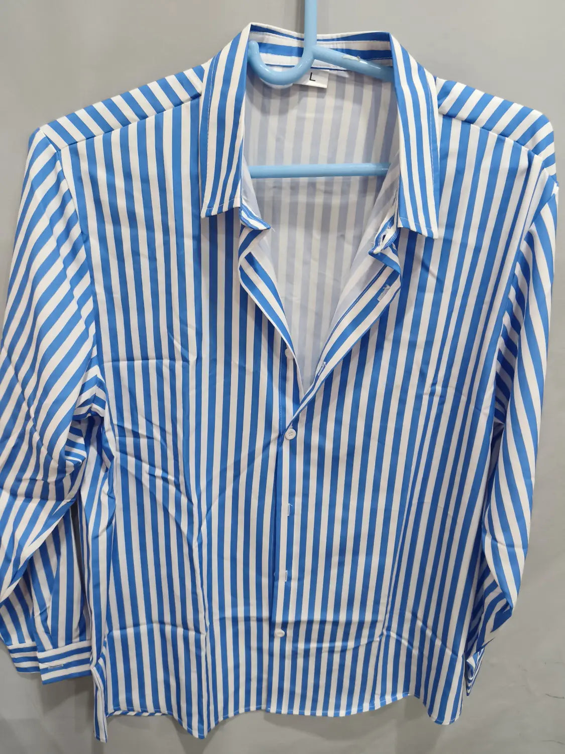 Chemise décontractée à manches longues rayée verticalement bleu et blanc pour hommes, suspendue sur un cintre.