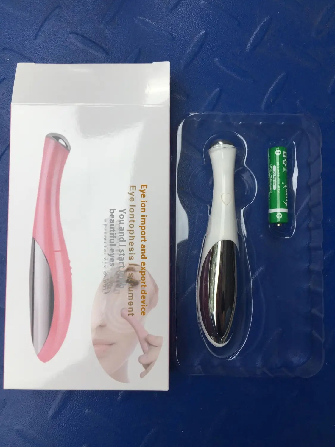 eye massager for wrinkle and dark circle removal with pink and silver eye ion导入 device in packaging including a green battery.