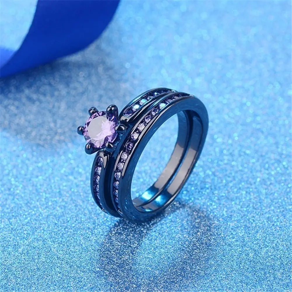 Elegant black tungsten wedding band set featuring a central lavender gemstone surrounded by smaller purple stones with an intricate design and metallic finish.