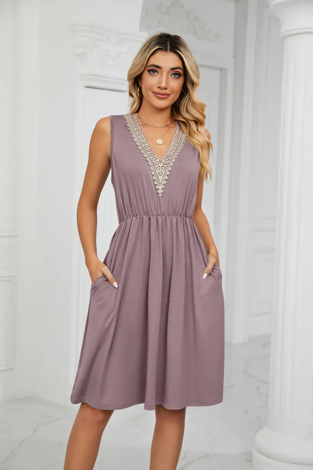 Ein ärmelloses mauves A-Linien-Kleid mit V-Ausschnitt, mit zarter weißer Spitzenverarbeitung und zwei Seitentaschen.