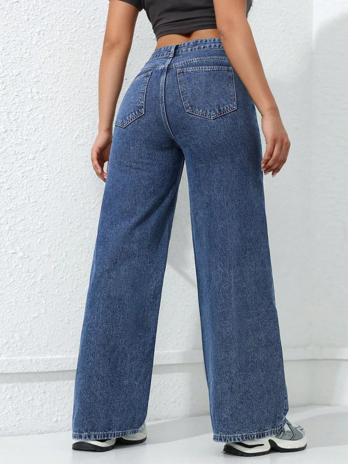 Jean à taille haute, jambe large et évasée, en denim bleu, présentant un design classique à cinq poches et un ourlet effiloché.