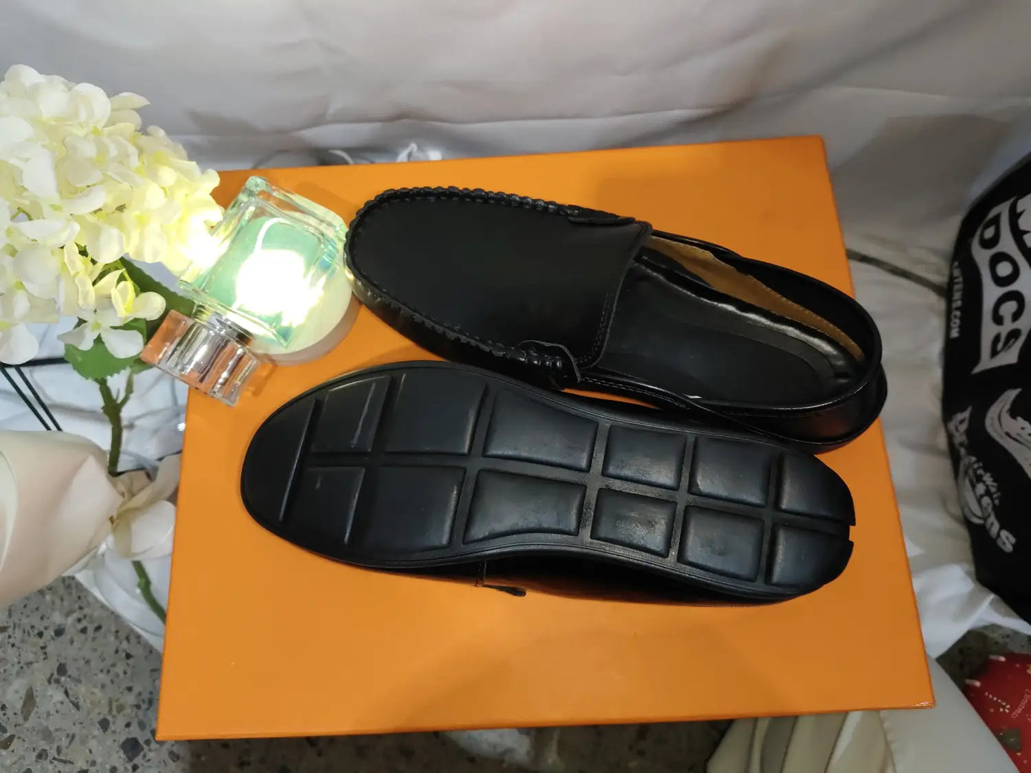 Mocasines tipo alpargata de cuero negro para hombre, con costuras cosidas y suela de goma texturizada, diseñados como zapatos de conducción casuales.