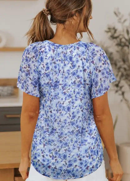 A light blue floral print summer blouse with gathered neckline and ruffled flutter sleeves.