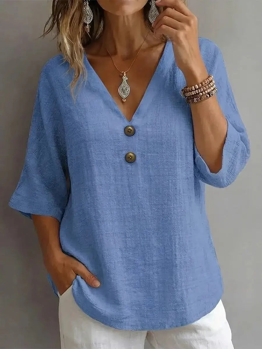 Light blue linen V-neck blouse with three-quarter sleeves and dark brown buttons.