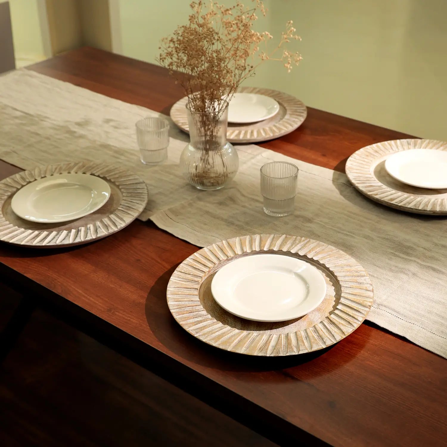 Ensemble de sous-assiettes en bois artisanal blanc, comprenant des assiettes en céramique blanches de 13 pouces, avec un motif d’éclats de soleil en relief sur le bord extérieur, dans une finition beige clair