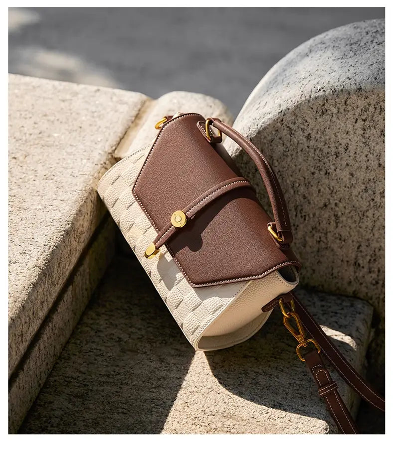 Eine stilvolle zweifarbige Webleder-Crossbody-Handtasche mit braunem Leder-Flip, cremefarbenem, strukturiertem Körper und goldtönigen Beschlägen.