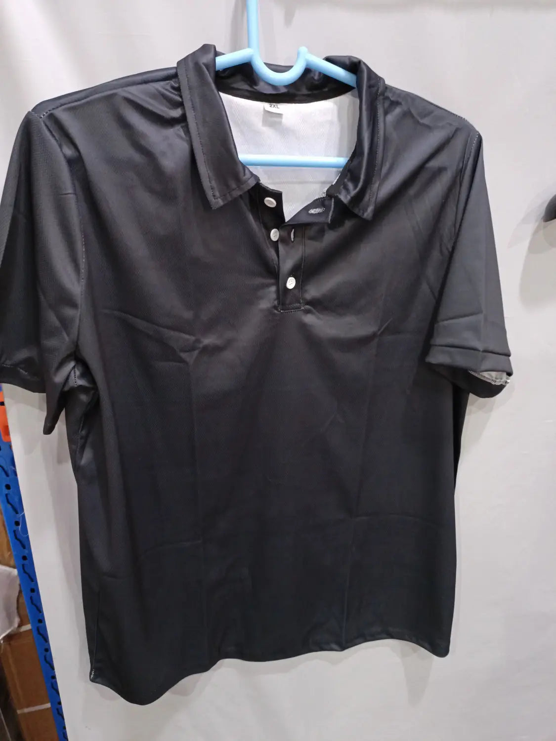 Herren-Cardigan mit kurzer Ärmellänge, strukturiert, mit Knopfleiste, schwarz, mit Kragen und weißen Knöpfen, die an einem blauen Bügel hängen.