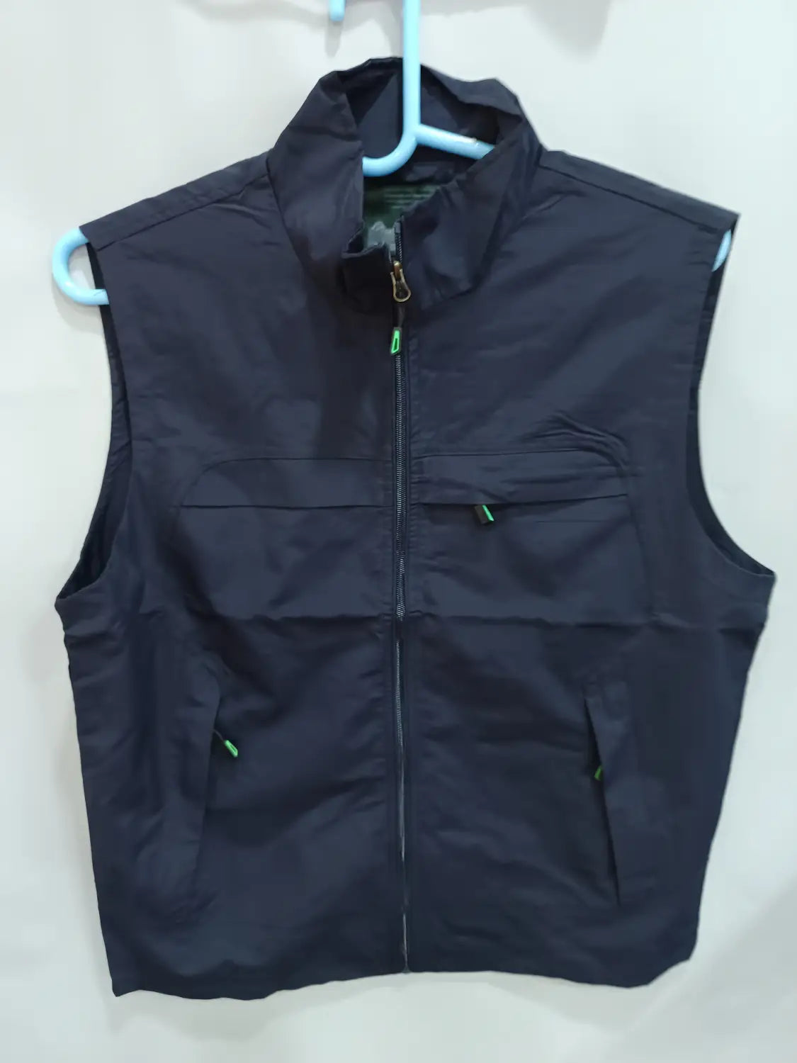 Chaleco utilitario impermeable negro de nailon con múltiples bolsillos, con tiradores verdes de la cremallera y bolsillos frontales.