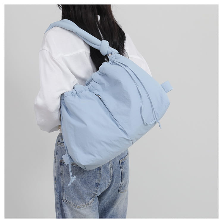 Light blue quilted puffer tote bag with a lightweight nylon shoulder design featuring a padded knotted drawstring strap and soft fabric finish.