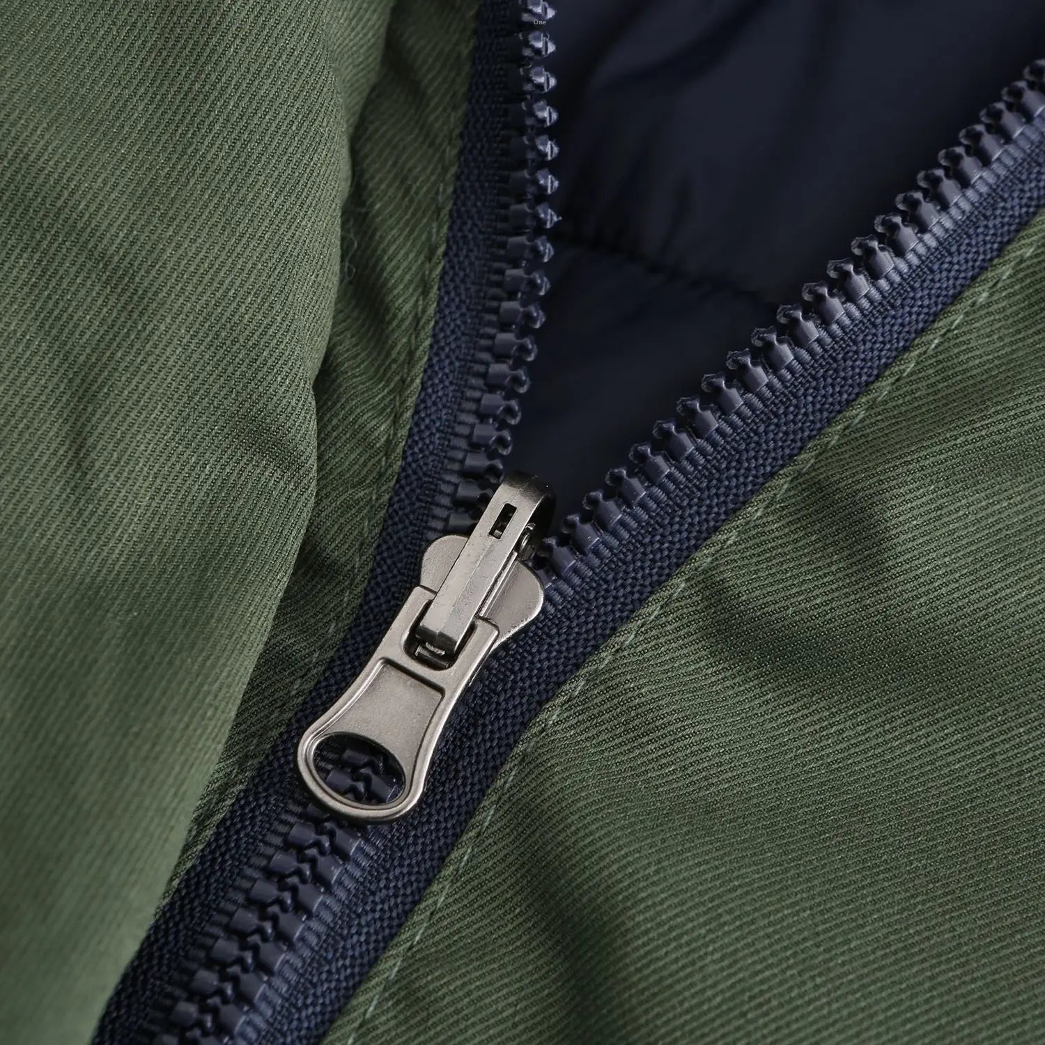 silver-toned zipper pull on a dark green textured fabric reversible fur collar quilted parka with navy blue inner lining.