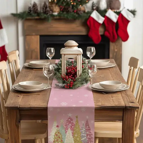 Chemin de table de Noël rose 13 × 72 présentant un motif festif de sapins de Noël colorés et de flocons de neige, avec une lanterne rustique en bois comme pièce centrale.