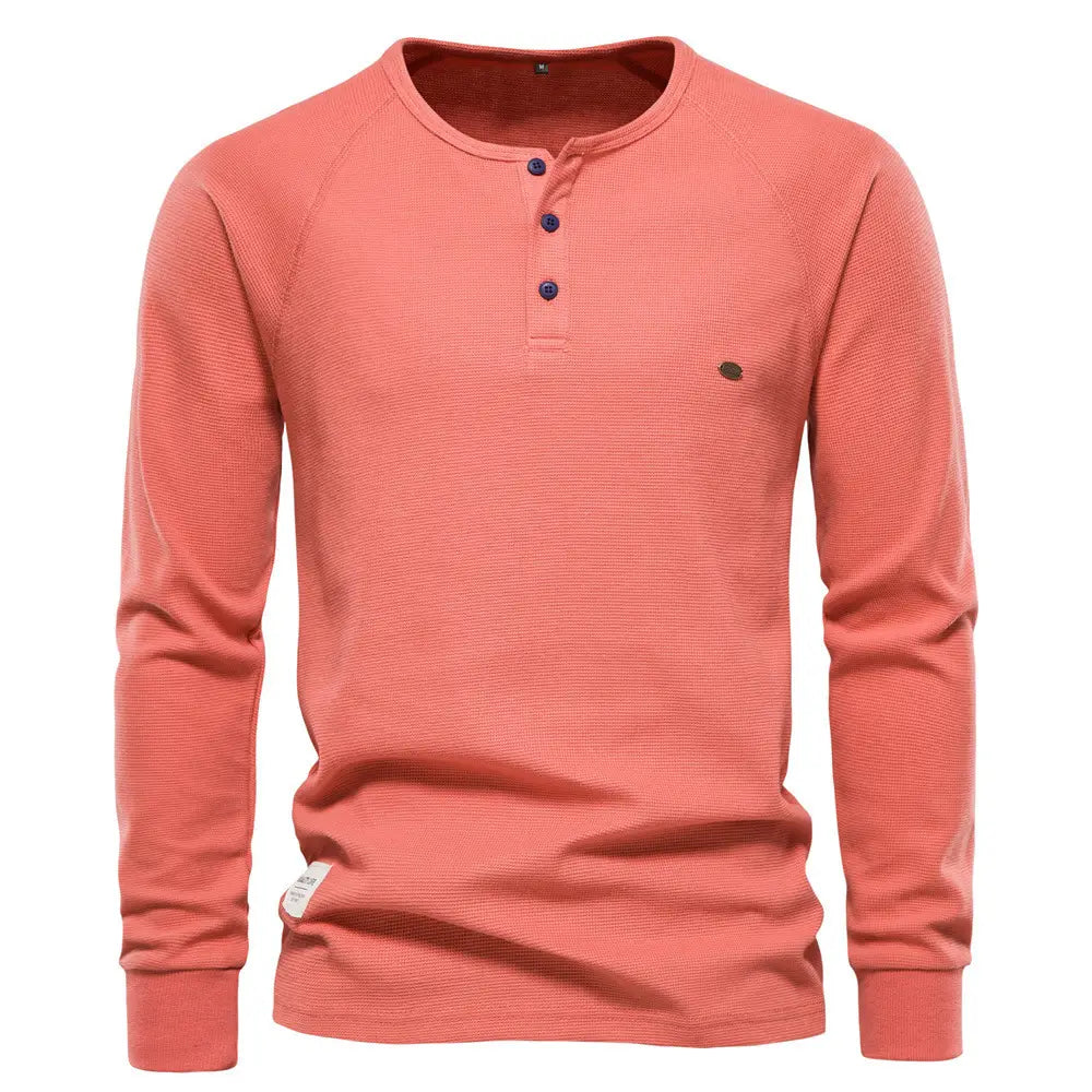 Chemise henley à manches longues côtelée pour homme, de couleur corail, présentant une texture côtelée et des boutons bleu foncé.