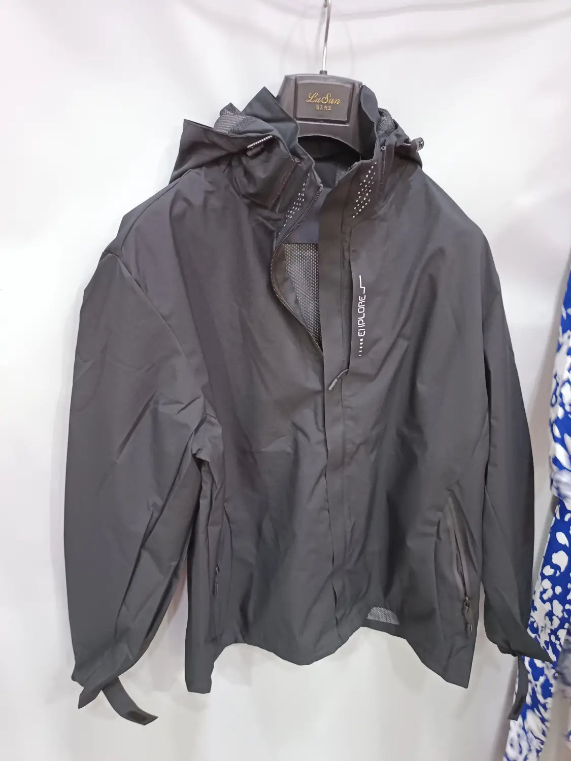 Black waterproof hiking jacket for men with a hood, mesh lining on the chest and underarms, zipper closure, side pockets, and a vertical brand logo embroidered on the left sleeve.