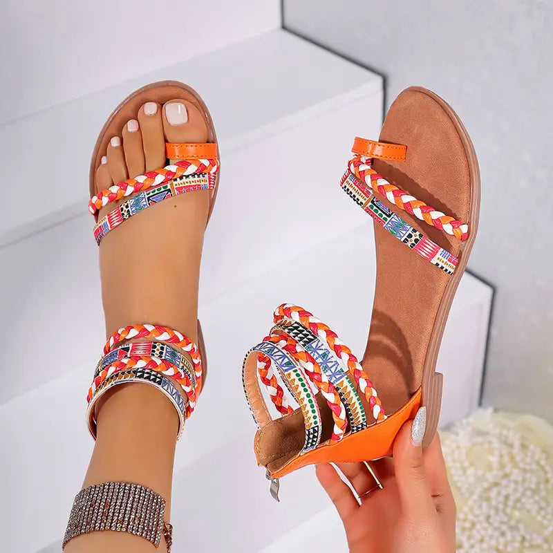 Bright orange and multicolored braided ankle strap flat sandals with patterned straps in a bohemian ethnic style.