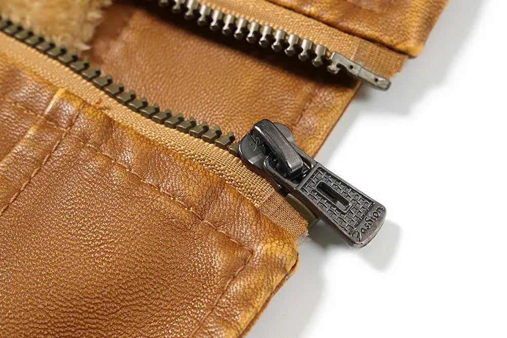 Primer plano de un tirador de cremallera de metal color bronce oscuro con logotipo en relieve sobre una tela de cuero color camel, en una chaqueta de invierno de forro polar de PU para hombre con capucha.