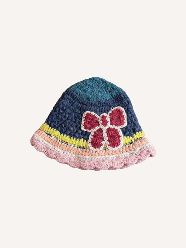 Un chapeau de pêcheur multicolore tricoté à la main en bleu marine, avec un dessus turquoise, comportant un nœud crocheté rouge et des bandes rayées colorées de jaune, rose et blanc le long du bord.