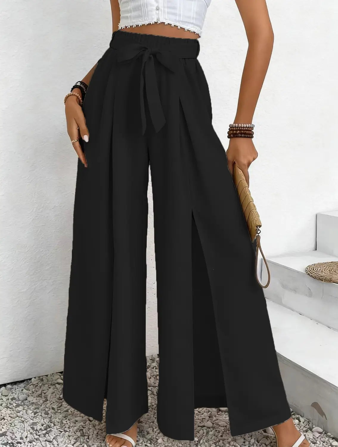 Pantalon ample à taille haute noir, avec une ceinture nouée et des fentes latérales, conçu comme un pantalon ample et décontracté.
