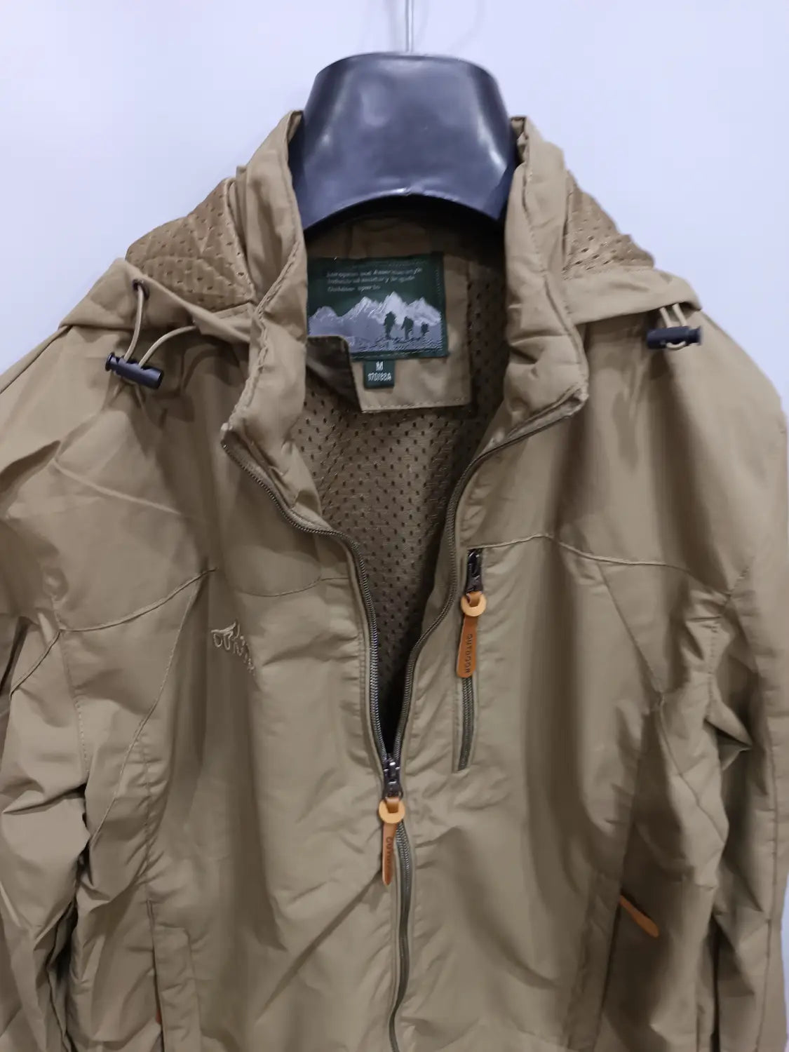 Chaqueta de senderismo con capucha impermeable color camel, con forro de malla y tiradores de cremallera de cuero, diseñada para actividades al aire libre.