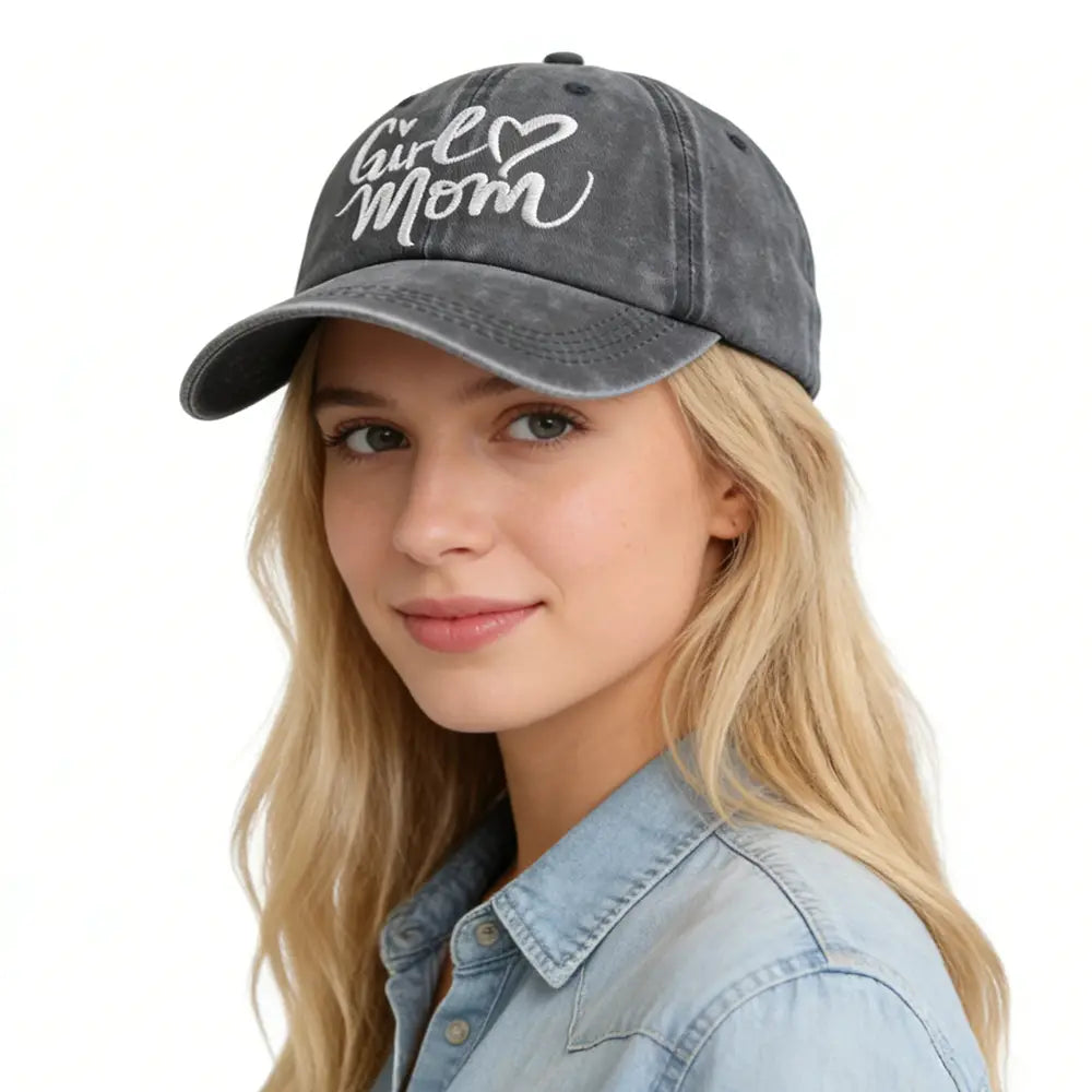 Une casquette de baseball réglable grise délavée à l’aspect vieilli avec l’inscription « girl mom » brodée en blanc en script cursif et un symbole en forme de cœur.