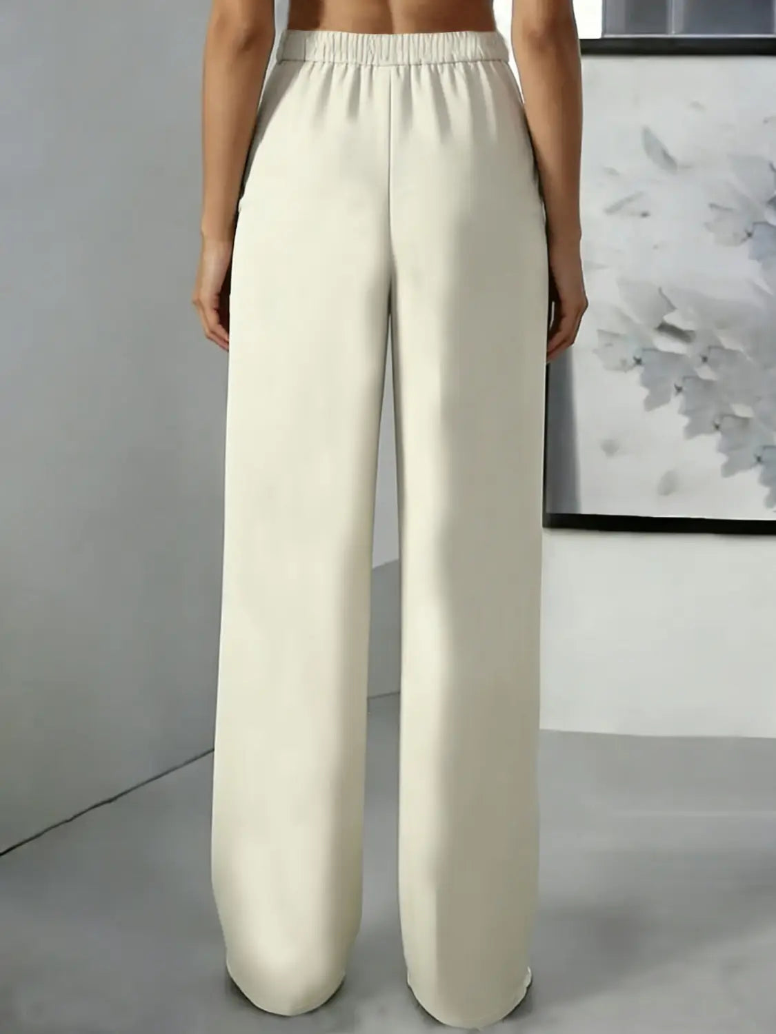 Pantalons taille haute à jambes larges couleur crème avec une ceinture élastique et un tissu lisse et fluide, conçus comme des pantalons plissés.