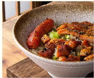 Eine rustikale, gesprenkelte japanische Keramikschale, gefüllt mit einer herzhaften Reiszubereitung, garniert mit knusprig gewürztem Hähnchen und Wurst.